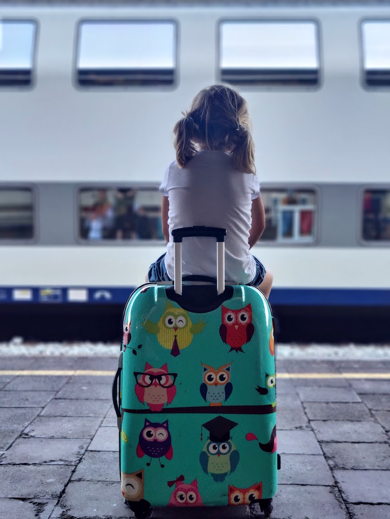 Een kind zit op een koffer op een perron en wacht op de trein